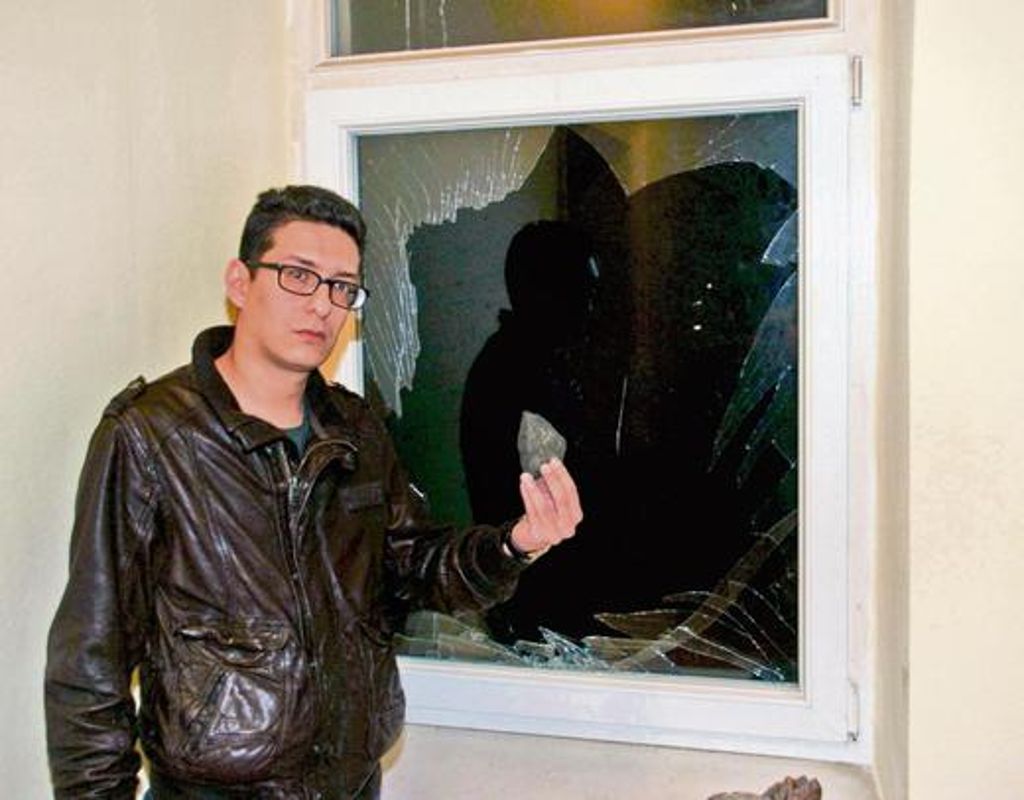 Amirabbas Omrani aus dem Iran zeigt vor einem zertrümmerten Fenster einen der Steine, die er zwischen den Scherben gefunden hat.